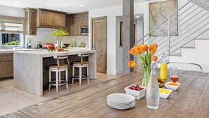 A modern kitchen with a marble island, wooden cabinets, and a dining area with a wooden table and chairs. - 200 East Balboa Oceanview Rooftop Steps to Sand, Pier, Boardwalk & Dining (Newport Beach)