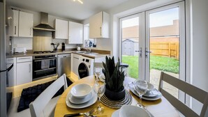 Een moderne keuken met witte kasten, een inbouwoven en een eethoek met een tafel gedekt voor twee personen.