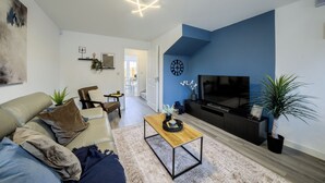 Een moderne woonkamer met een bank, salontafel en een flatscreen televisie tegen een blauwe accentmuur.