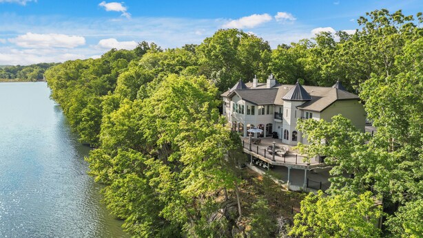A large house with a balcony overlooking a lake, surrounded by dense trees.