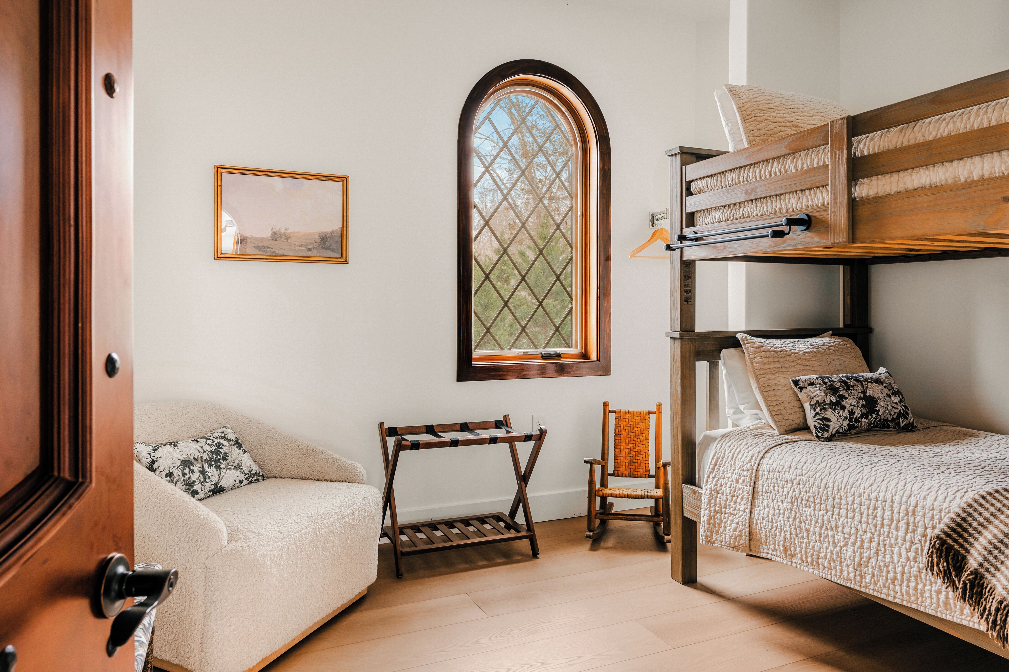 Una camera da letto con un letto a castello, una poltrona, una sedia, una mensola in legno e una finestra con vista.