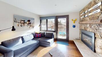 A modern living room with a sectional sofa, a fireplace, a ski-themed artwork, and a stone wall.