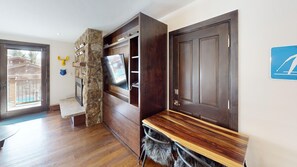 A room with a stone accent wall, a flat-screen TV, a wooden bench, and a door with a ski icon.