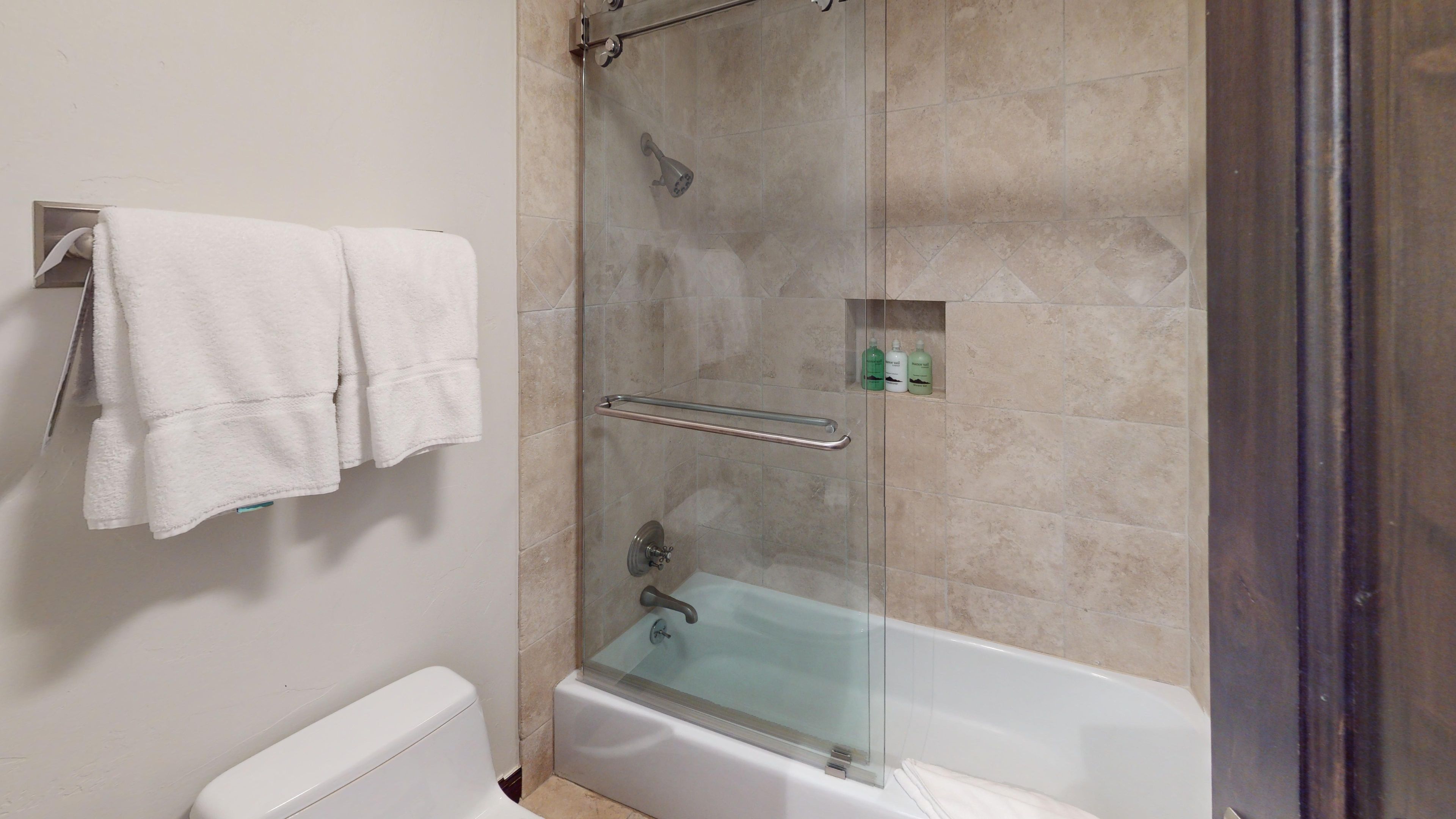 A bathroom with a glass-enclosed shower, a white bathtub, and a towel rack with two towels.