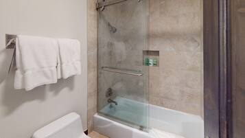 A bathroom with a glass-enclosed shower, a white bathtub, and a towel rack with two towels.