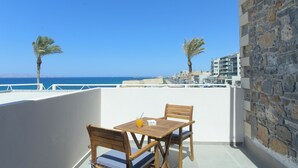 A balcony with a wooden table and chairs, a drink, and a view of the sea and buildings.