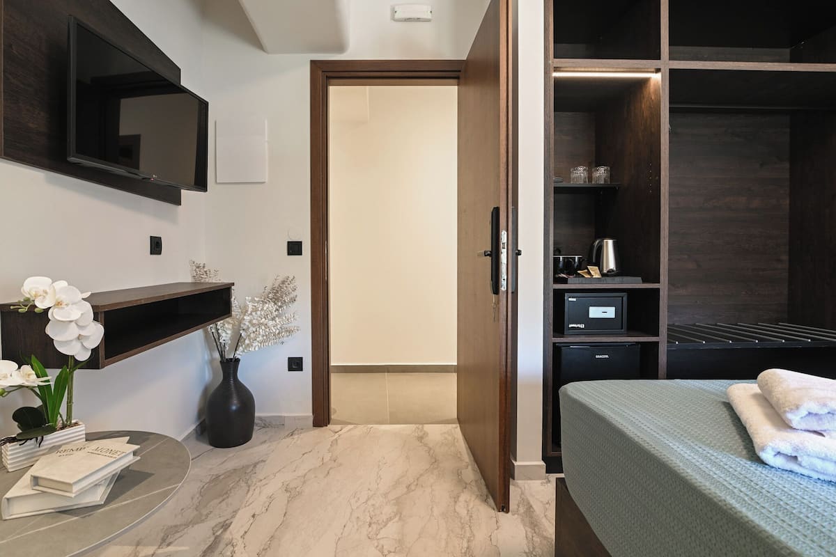 A modern bedroom with a bed, a vanity with a mirror, a TV mounted on the wall, a small table with books and flowers, and a closet with shelves.