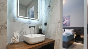A modern bathroom with a marble backsplash, a white sink, and a wooden vanity. - Envy Seaside Suites (Heraklion)