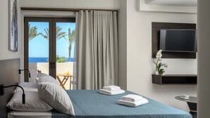 A hotel room with a bed, a TV mounted on the wall, and a view of the ocean through the window. - Envy Seaside Suites (Heraklion)