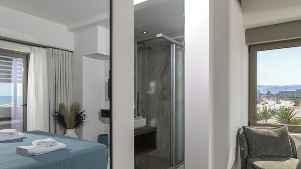 A modern hotel room with a bed, a shower area, a balcony with a view, and a seating area.