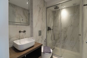 A modern bathroom with a marble sink, a glass shower enclosure, and a toilet. - Envy Seaside Suites (Heraklion)