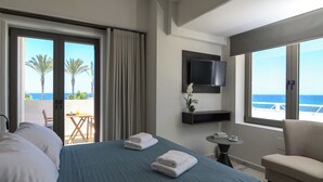 A hotel room with a bed, a TV, a small table, a chair, and a balcony with a view of the sea. - Envy Seaside Suites (Heraklion)