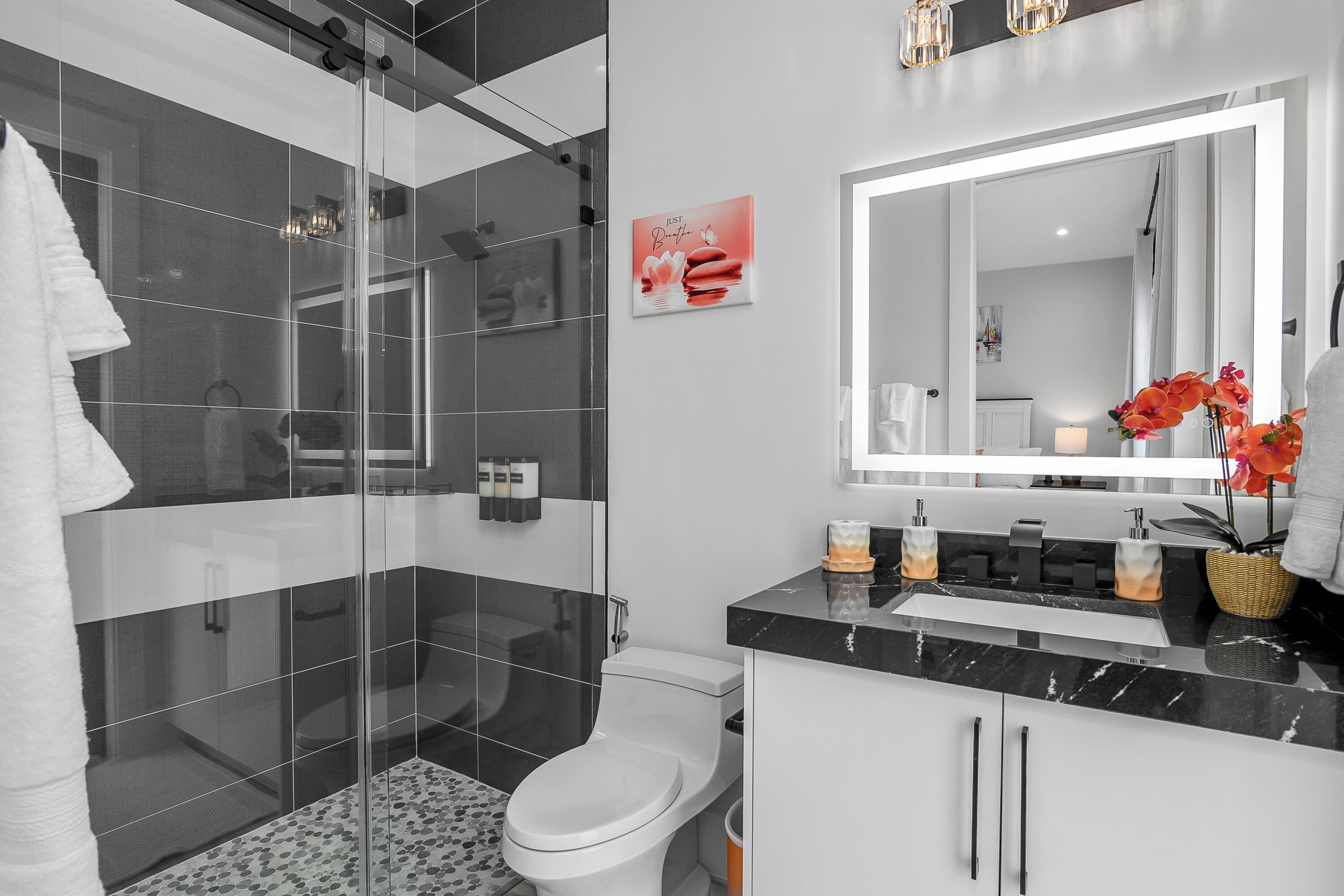 Une salle de bain moderne avec une douche à parois de verre, des toilettes blanches et un lavabo en marbre noir.