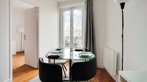A dining area with a glass table, black chairs, and a view of a balcony through a window. - Chic apartment - 1BR/4P - Next to Paris (Saint-Ouen-sur-Seine)
