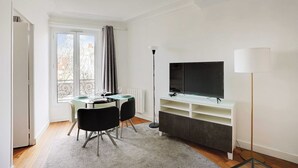 A modern living room with a dining area, a flat-screen TV, and a floor lamp. - Chic apartment - 1BR/4P - Next to Paris (Saint-Ouen-sur-Seine)