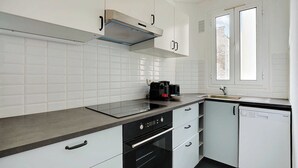 A modern kitchen with white cabinets, a black countertop, a built-in oven, and a dishwasher. - Chic apartment - 1BR/4P - Next to Paris (Saint-Ouen-sur-Seine)
