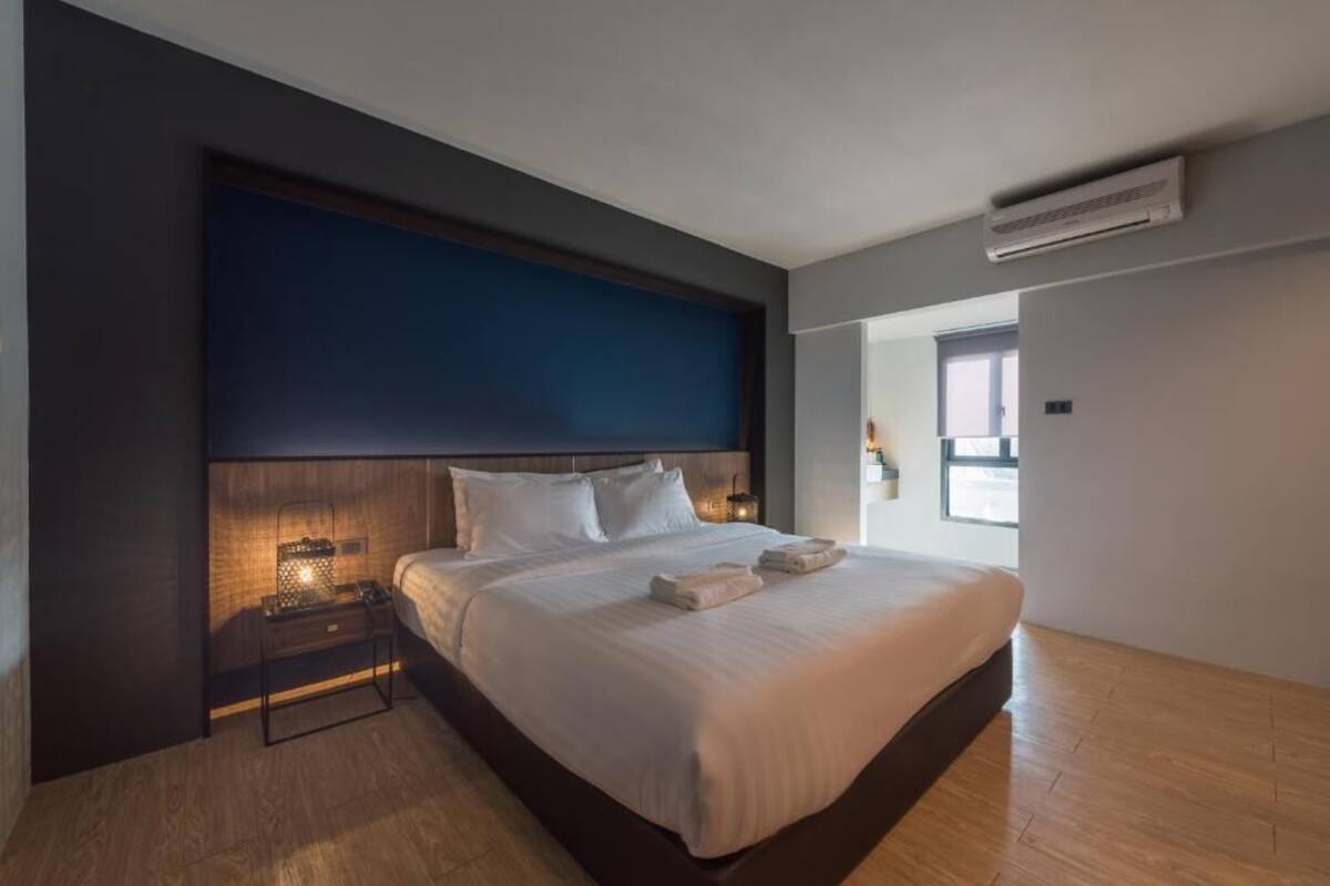 A modern hotel room with a large bed, a bedside table with a lamp, and an air conditioning unit on the wall.