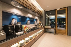 Una cocina de hotel moderna con una encimera larga, ollas negras y platos apilados ordenadamente.