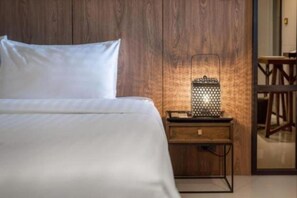 Una cama bien hecha con cubrecama y almohadas blancas, una mesita de noche de madera con lámpara de metal y un panel de pared de madera.
