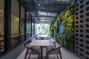An indoor dining area with a long table and benches, a ceiling with a grid pattern, and a wall with vertical greenery. - L Nimman Boutique Hotel (Chiang Mai)