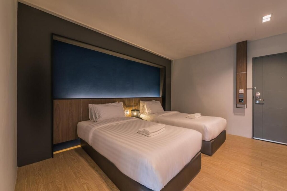 A modern hotel room with two beds, a dark accent wall, and a wooden floor.