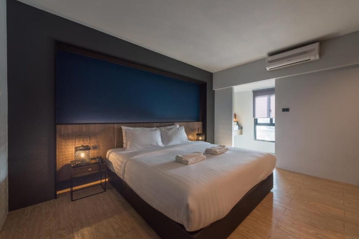 A modern hotel room with a large bed, a bedside table with a lamp, and an air conditioning unit on the wall.