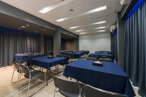 Un salón de conferencias con varias mesas y sillas, equipado con iluminación en el techo y cortinas.