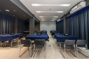 Un salón de conferencias con mesas, sillas, unidades de aire acondicionado y cortinas.