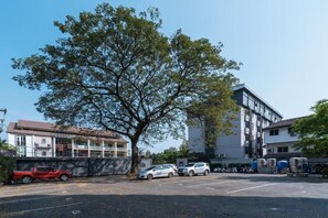 A parking lot with several cars, a large tree, and buildings in the background. - L Nimman Boutique Hotel (Chiang Mai)
