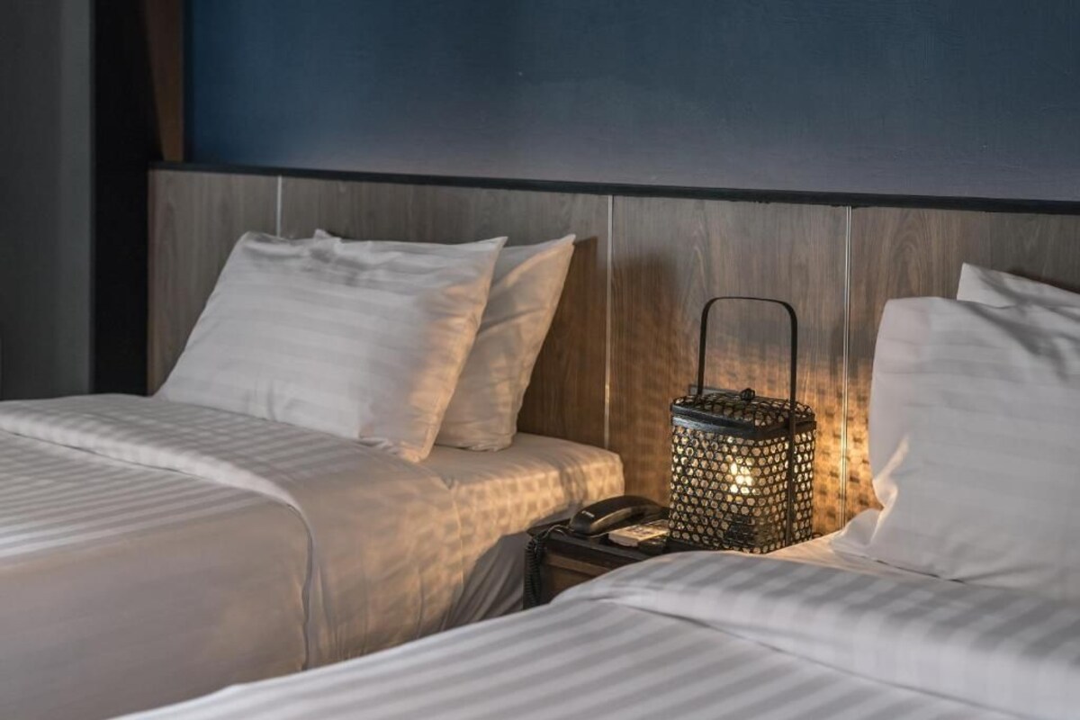 Habitación de hotel con cabecera de madera, dos camas con sábanas blancas y un farol decorativo en la mesita de noche.
