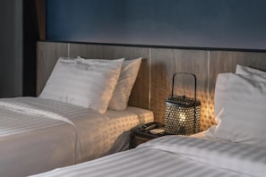 Habitación de hotel con cabecera de madera, dos camas con sábanas blancas y un farol decorativo en la mesita de noche.