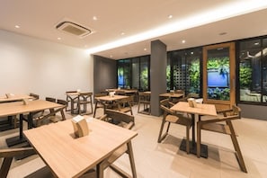 Un comedor moderno con mesas y sillas de madera, amplias ventanas con vista a zonas verdes e iluminación empotrada en el techo.