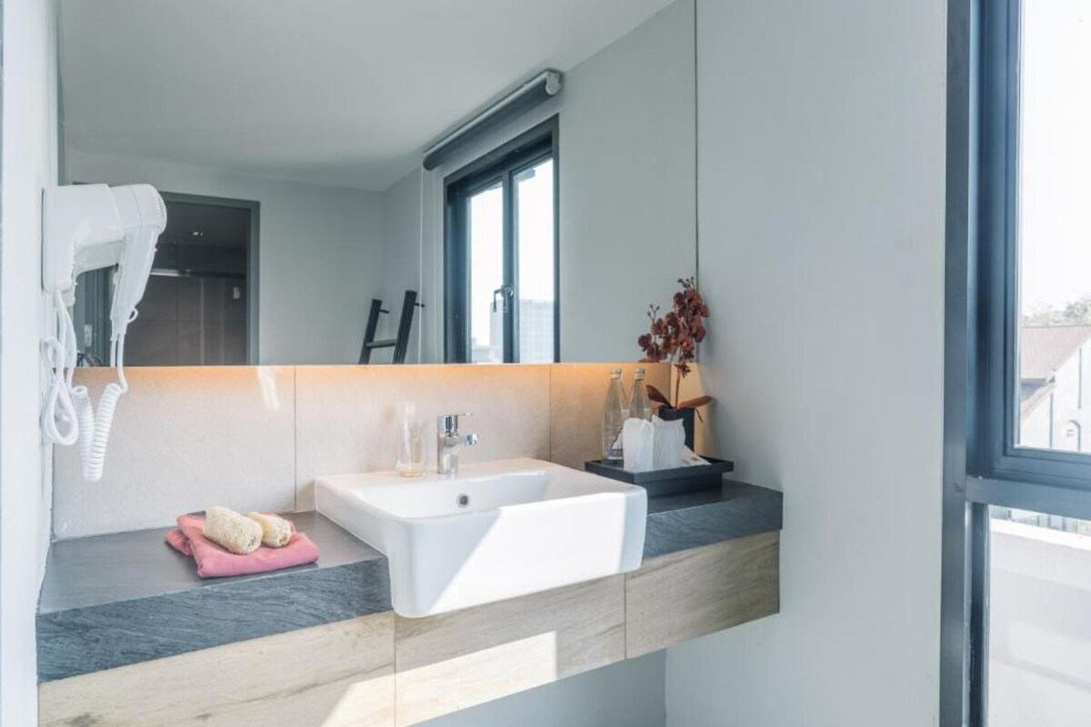 Un baño moderno con un espejo grande, un lavamanos blanco y un perchero para toallas.