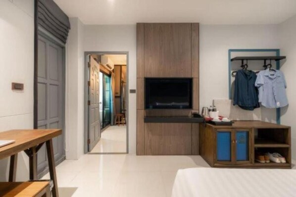 Una habitación de hotel moderna con un armario de madera, un televisor de pantalla plana, un escritorio y un perchero.