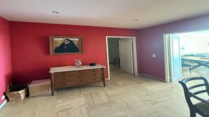 Une pièce avec une commode en bois, un tableau encadré au mur et une porte donnant sur une autre pièce.