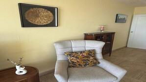 Un salon avec un fauteuil gris, une petite table d’appoint en bois sur laquelle se trouve un vase, et une œuvre d’art encadrée accrochée au mur.