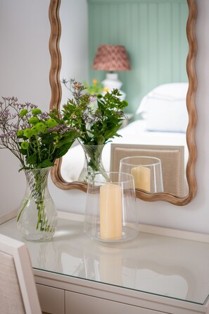 Un tocador de baño con espejo, dos jarrones de vidrio con flores y dos velas.