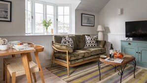 A cozy living room with a wooden dining table, a sofa with patterned cushions, a television, and a window with a view of the city.