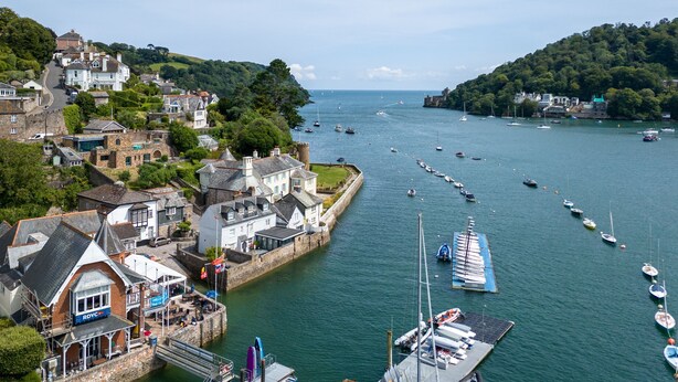 A coastal town with historic buildings, a marina with boats, and a castle on a hill.
