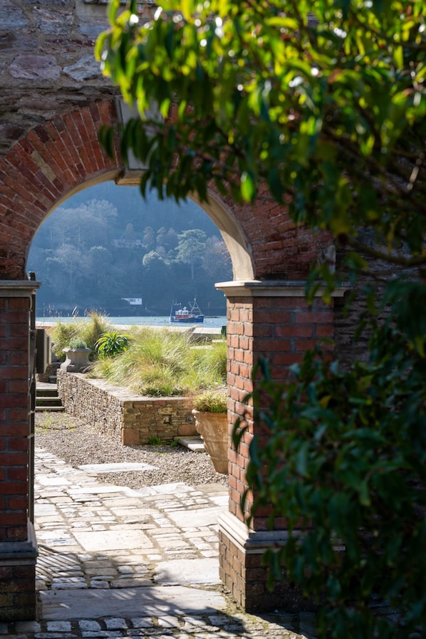 A stone pathway leading to a brick archway overlooking a body of water with a boat.