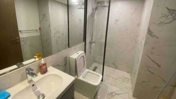 Un baño moderno con cabina de ducha revestida de mármol, inodoro y lavabo con espejo.