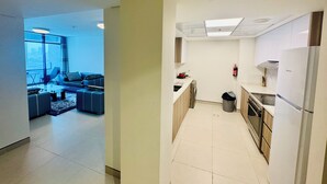 A modern apartment with a living area featuring a sofa, coffee table, and a view of the city. The kitchen includes a refrigerator, stove, and a washing machine. - Wow Amazing BurjKhalifa Sea SunSet Ship (Dubai)