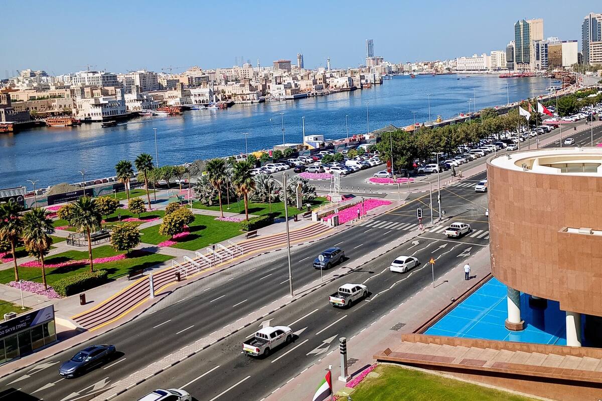 Un paisaje urbano con un río, edificios modernos y una carretera con coches.
