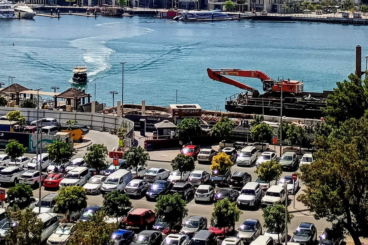 Un paisaje urbano con un puerto deportivo, barcos y una grúa.