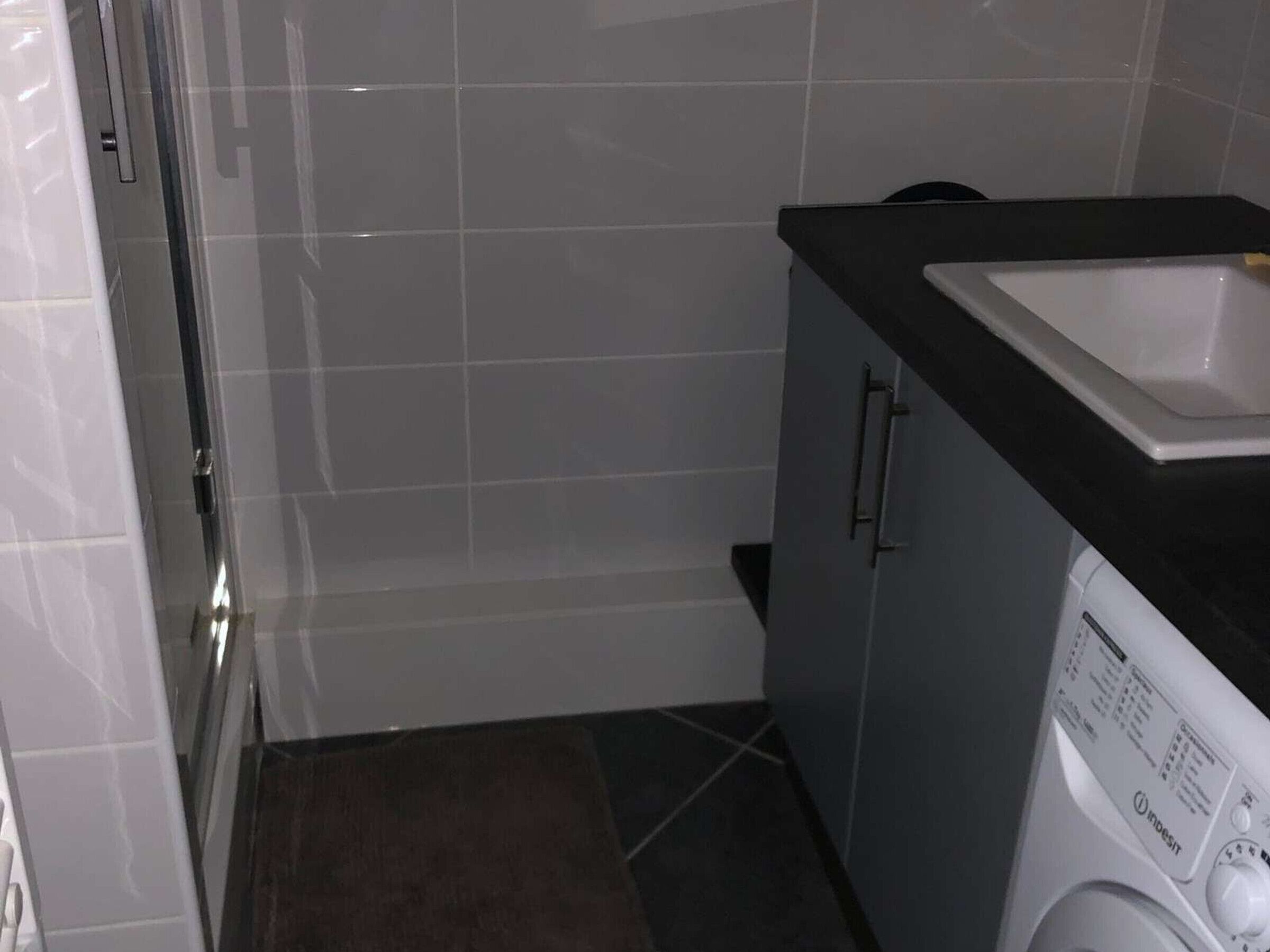 Un baño pequeño con ducha, lavabo y lavadora.