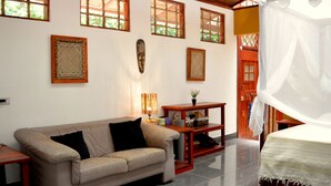 A room with a sofa, a bed with a canopy, a small table, and a wall with framed artwork. - Villa 5 - Modern 2 Bed Villa in Playa Chiquita (Cahuita)