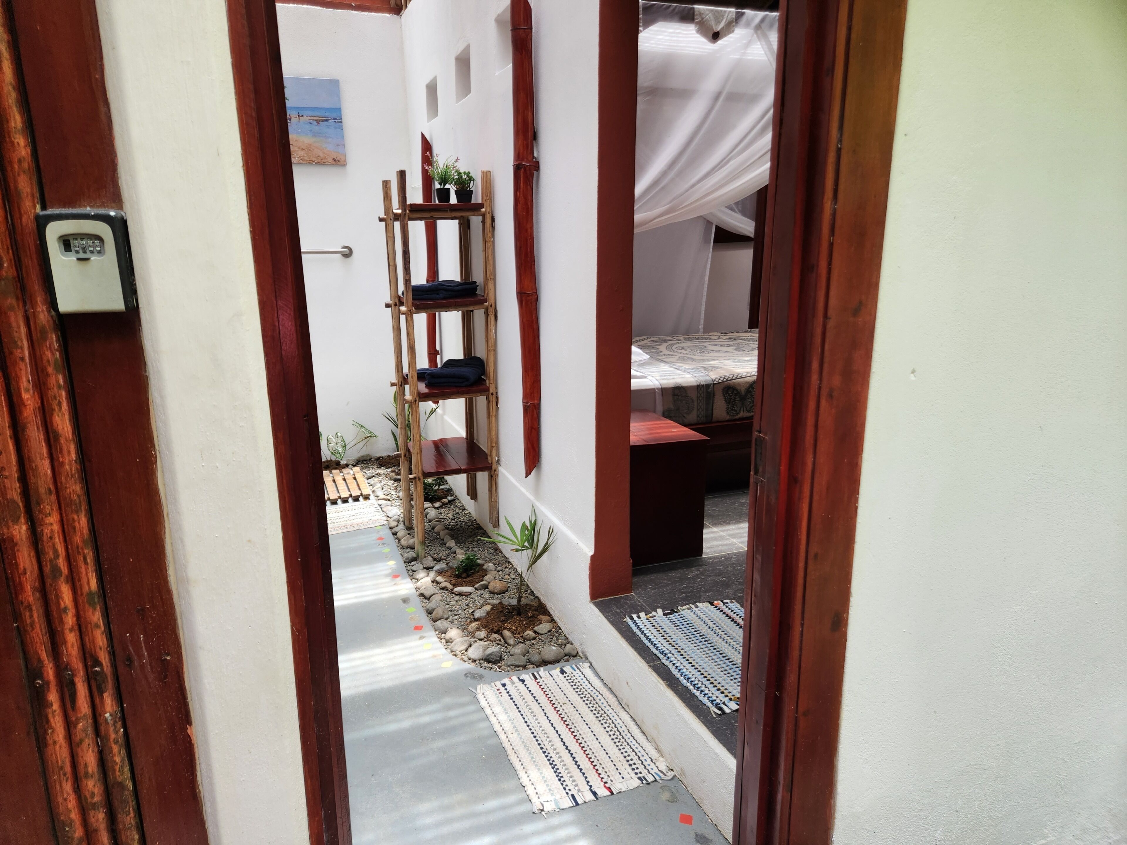 Um corredor estreito com escada de madeira, uma cama com colcha estampada e uma pequena mesa.