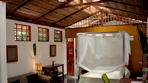 A room with a bed, a sofa, a wooden desk, a computer, and a window with a view of greenery. - Villa 5 - Modern 2 Bed Villa in Playa Chiquita (Cahuita)