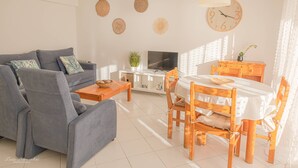 A living room with a grey sofa, a wooden dining table with chairs, a TV, and a clock on the wall. - Apartament Sea view Concorde (Portimão)