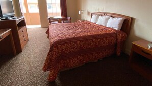 A hotel room with a large bed, a desk with a television, a chair, and a window with curtains. - Travel Inn San Antonio (San Antonio)
